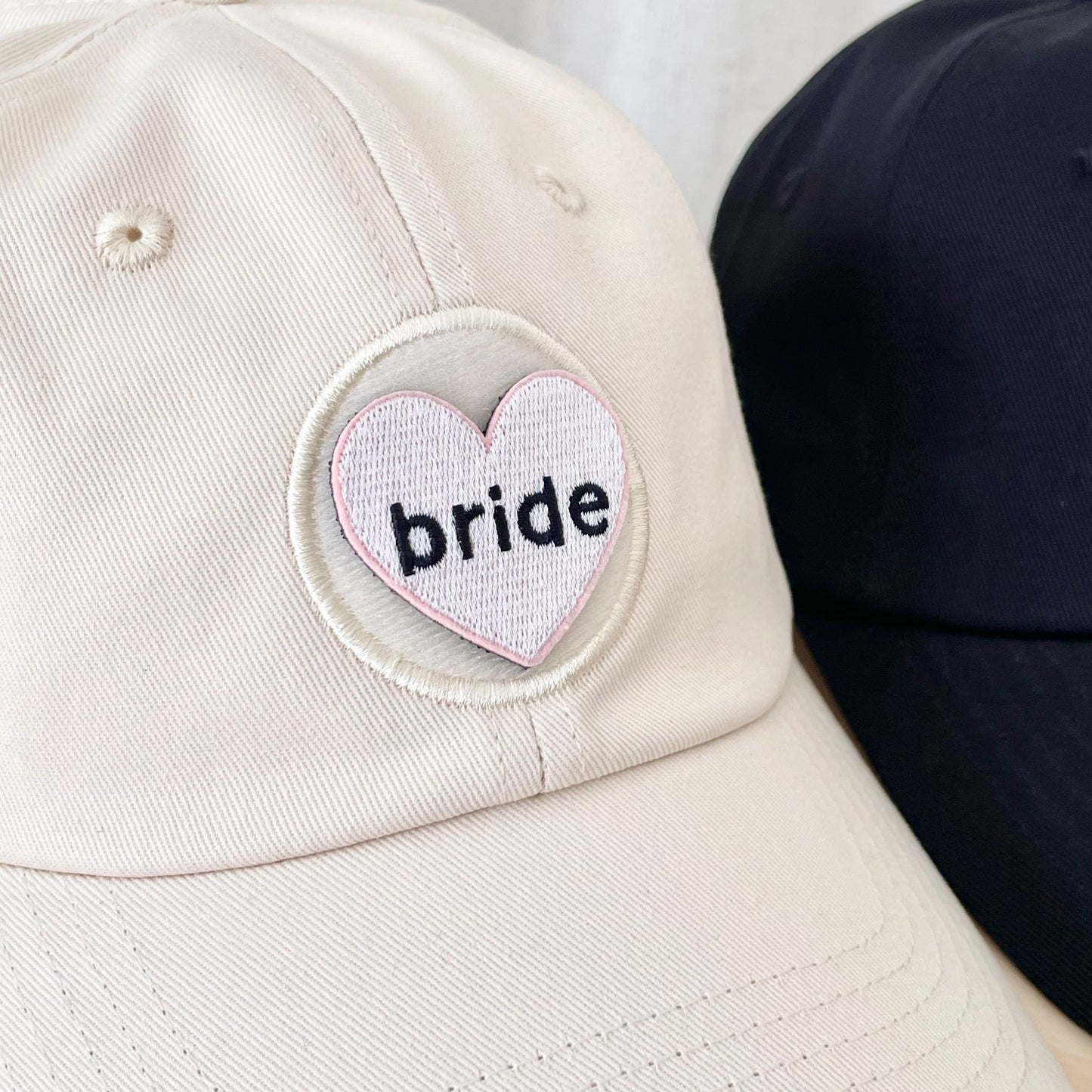 close up of a cream hat with a white heart shaped velcro patch that says "bride"