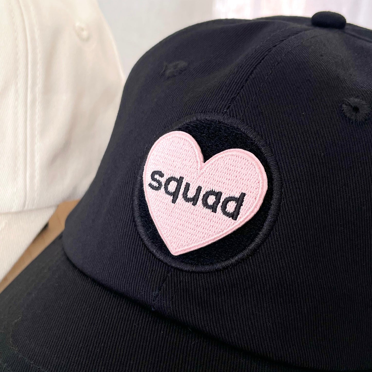 close up of black hat with pink shaped heart velcro embroidered patch with text that says "squad"