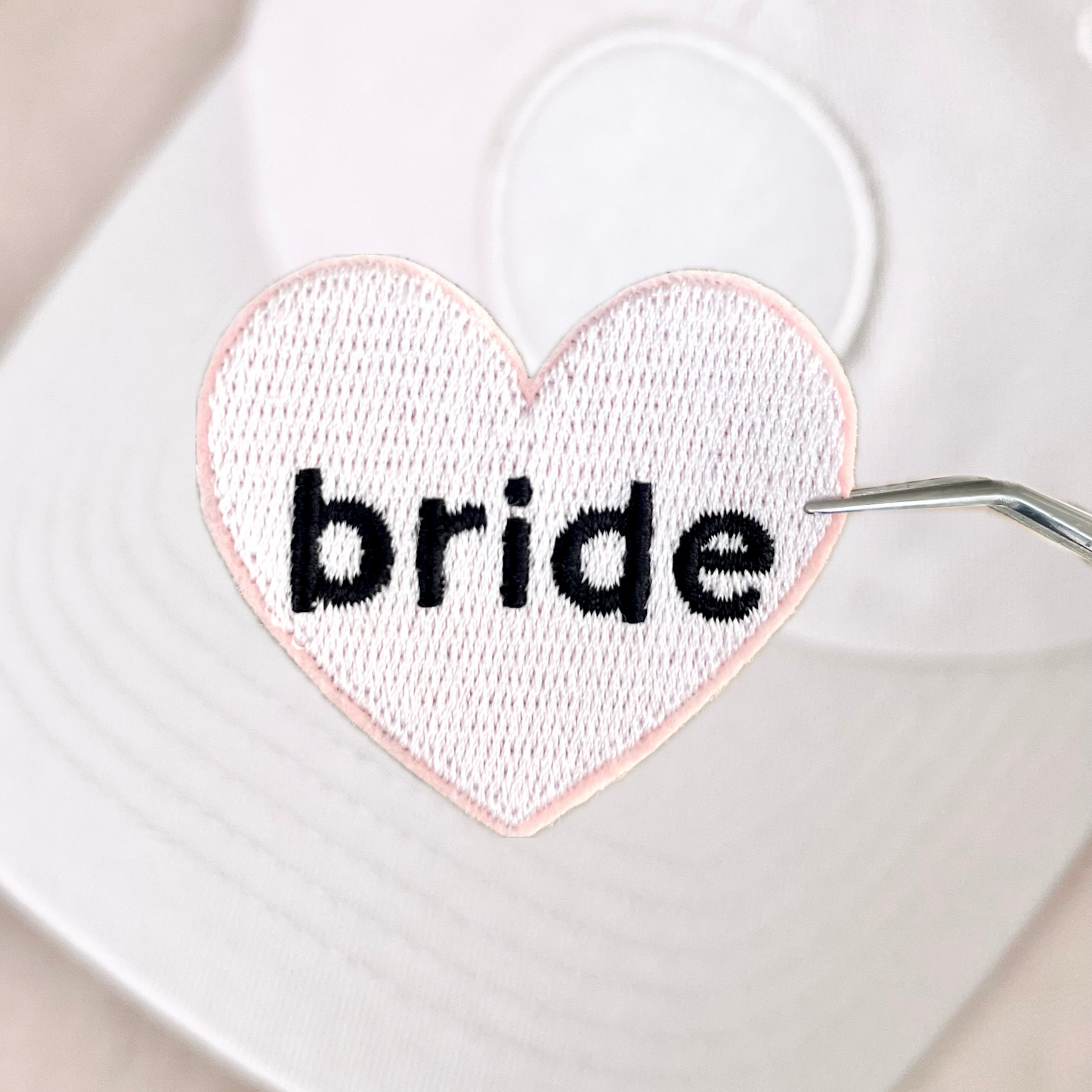 A white heart-shaped velcro patch with the word 'bride' embroidered in the center, against a neutral background.