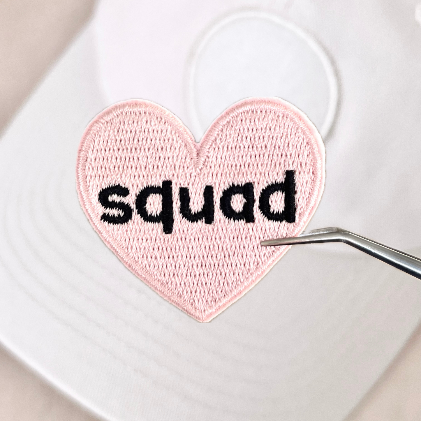 A pink heart-shaped velcro patch with the word 'squad' embroidered in the center, displayed on a white background.