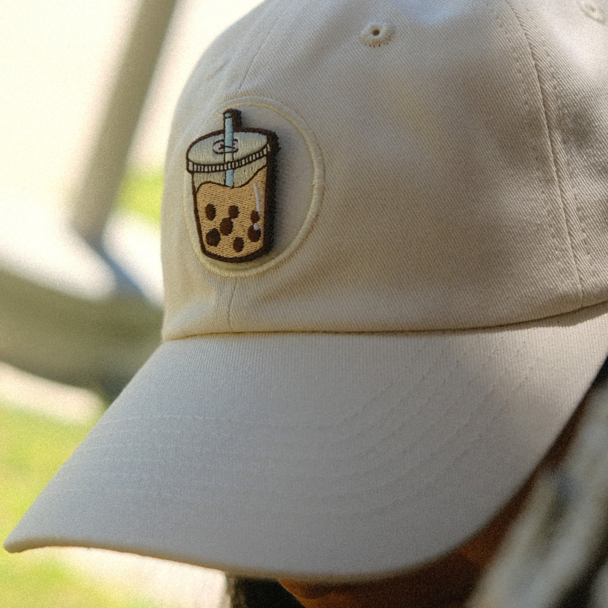 Beige cap with a bubble tea design patch on a blurred outdoor background